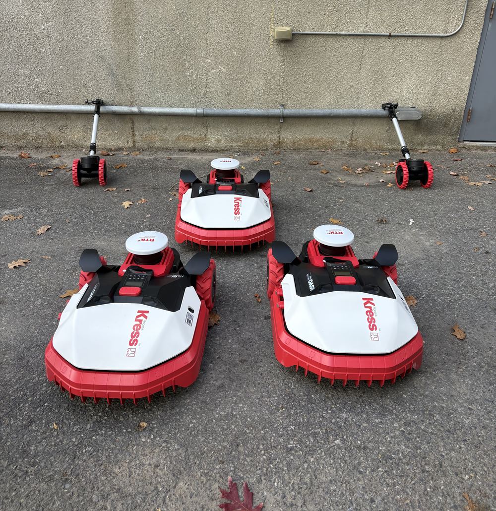 Three Kress RTK robots lined up outside a maintenance building